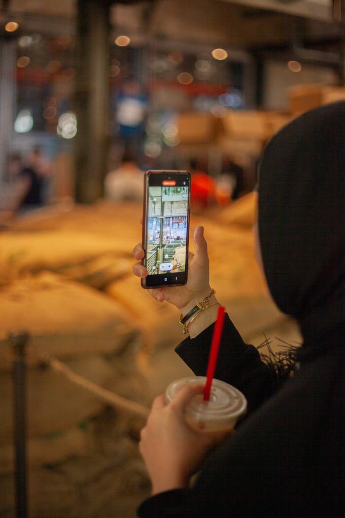 A woman using a smartphone while holding a drink inside a coffee shop.